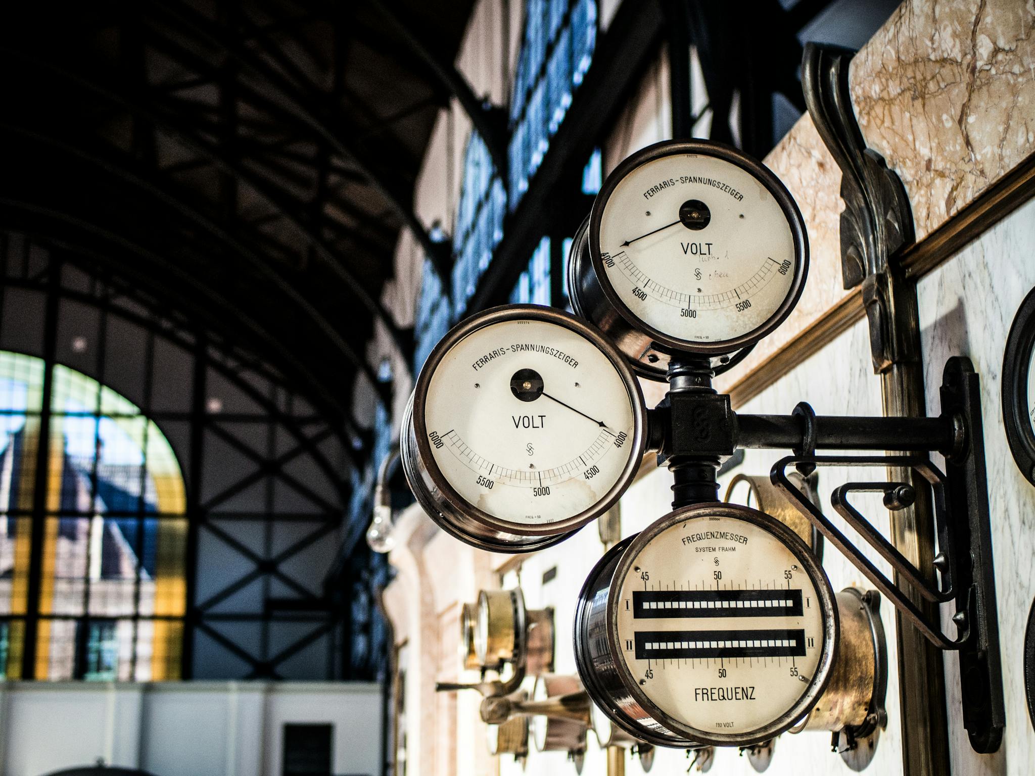 Intricate vintage volt and frequency gauges in an industrial setting with blurred background.